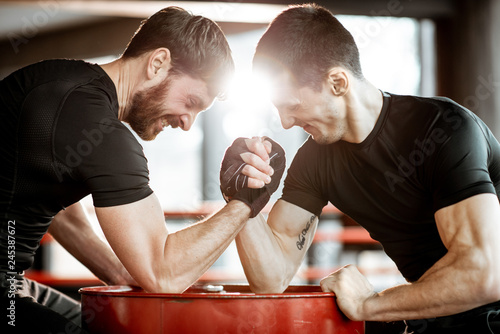 Two young athletes in black sportswear having a hard arm wrestling competition on a red barrel in the gym photo