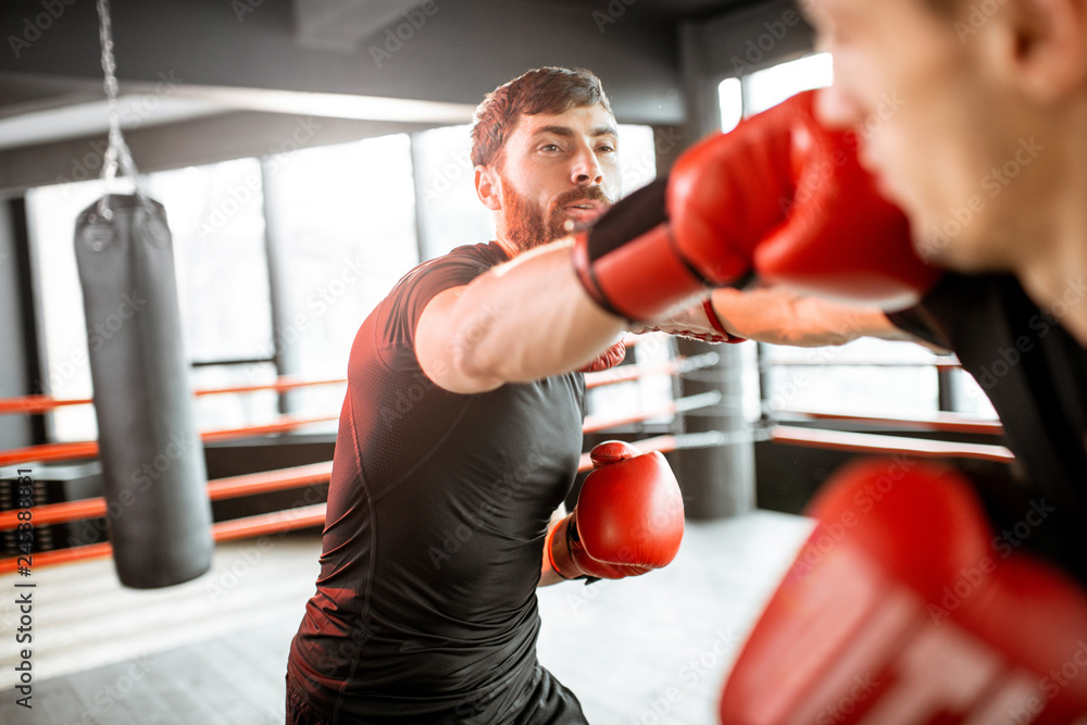 Two professional boxers in black sportswear during the fight on the boxing ring at the gym