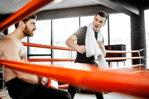 Boxing trainer giving instructions during a break motivating a boxer sitting on the corner of the boxing ring