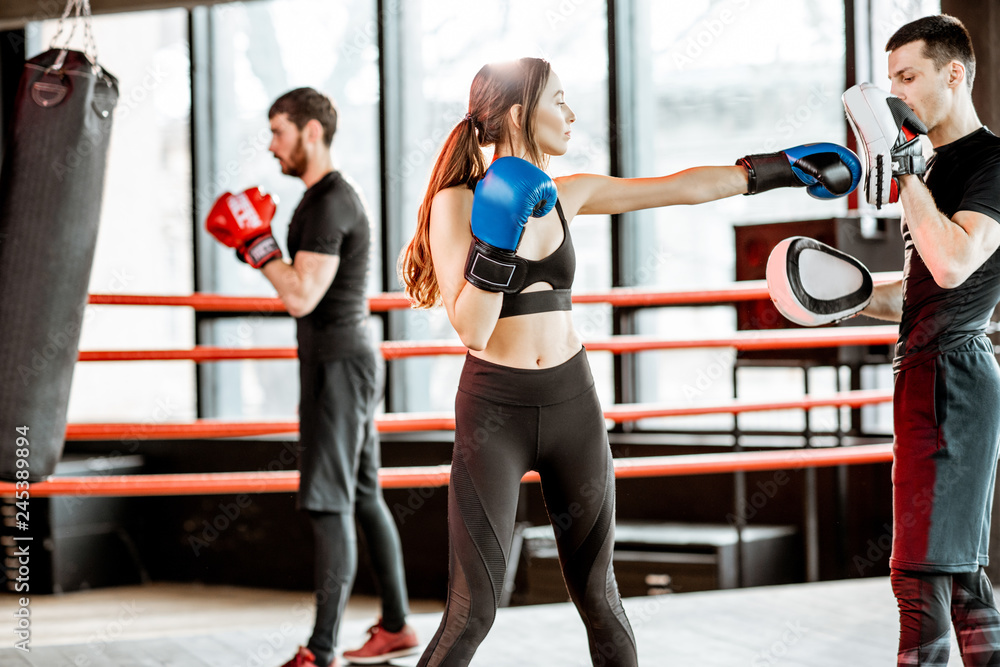 Fototapeta Młoda kobieta trenuje boksować z osobistym trenerem na bokserskim ringu przy gym