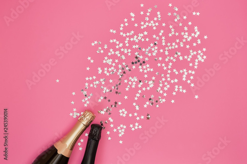 Champagne bottles with confetti stars on pink background. Copy space, top view
