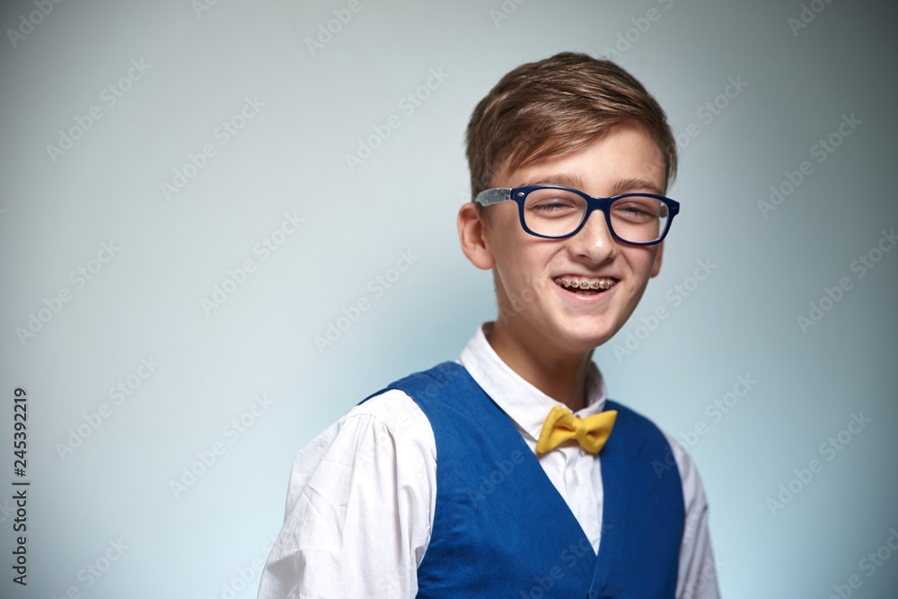 Boy teenager with braces in glasses. Wearing a shirt with a bow tie. On the teeth of dental braces.