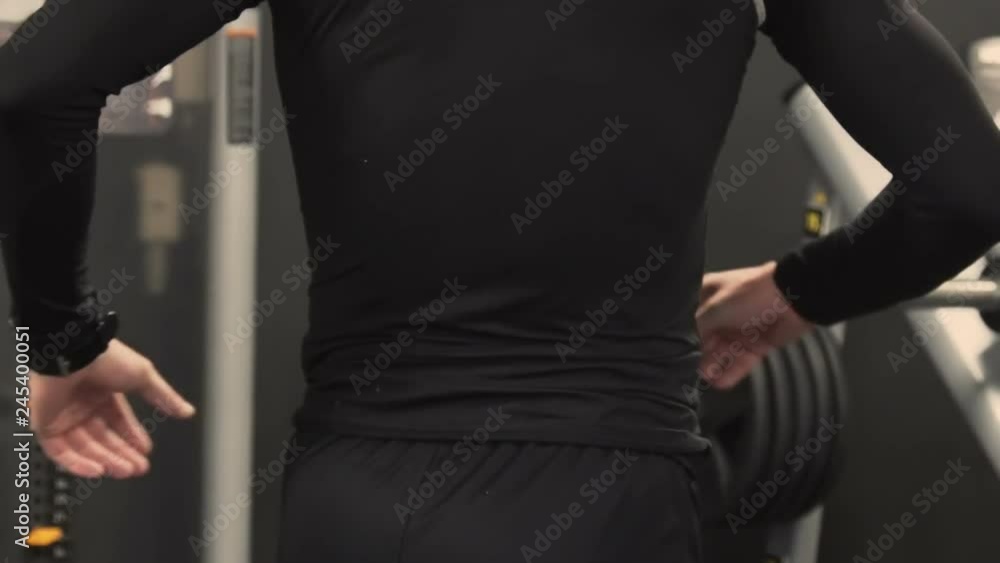 Side view of athletic handsome young man with beard in black sportswear stretching back muscles after exercising in gym, pressing hands against lower back, bending. Health concept Side view of athletic handsome young man with beard in black sportswear stretching back muscles after exercising in gym, pressing hands against lower back, bending. Health concept