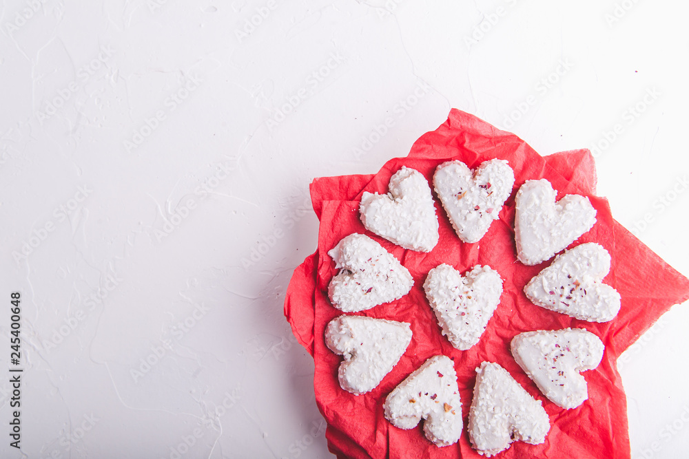White heart shaped Valentine's day cookies with white glaze and coconut flakes on a red napkin. Copy space. Flat lay