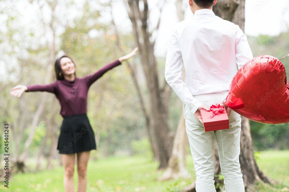 Young woman receiving a surprise gift red box from her boyfriend in the garden. boyfriend hide the gift and balloon