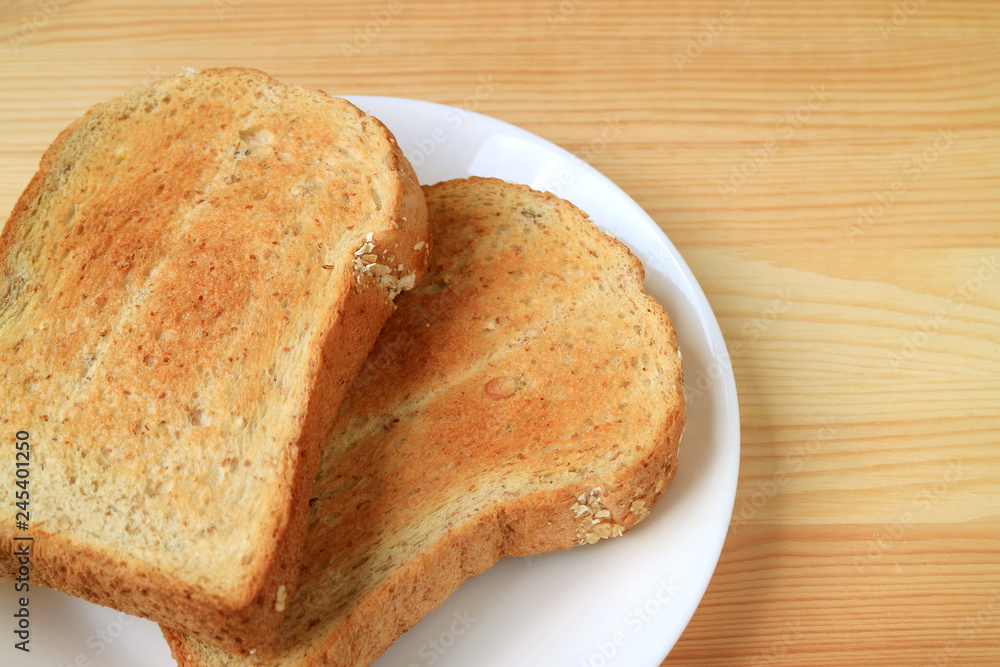 Two pieces of toasted whole wheat multigrain sliced bread on white plate served on wooden table Two pieces of toasted whole wheat multigrain sliced bread on white plate served on wooden table