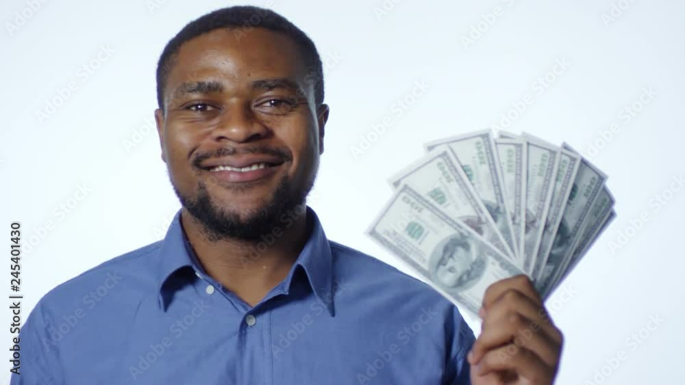 Happy african american man holding hundred dollar banknotes fan, nodding head and smiling at camera while posing against white background in studio Happy african american man holding hundred dollar banknotes fan, nodding head and smiling at camera while posing against white background in studio