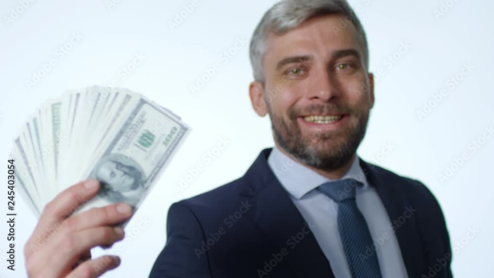 Rack focused shot of joyous middle aged businessman showing hundred dollar bills fan at camera and smiling while posing in studio with white background Rack focused shot of joyous middle aged businessman showing hundred dollar bills fan at camera and smiling while posing in studio with white background