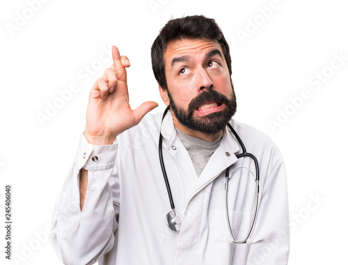 Young doctor with his fingers crossing on white background © luismolinero