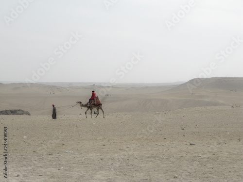 Bedouin carries tourist on a camel through the desert on a hot day