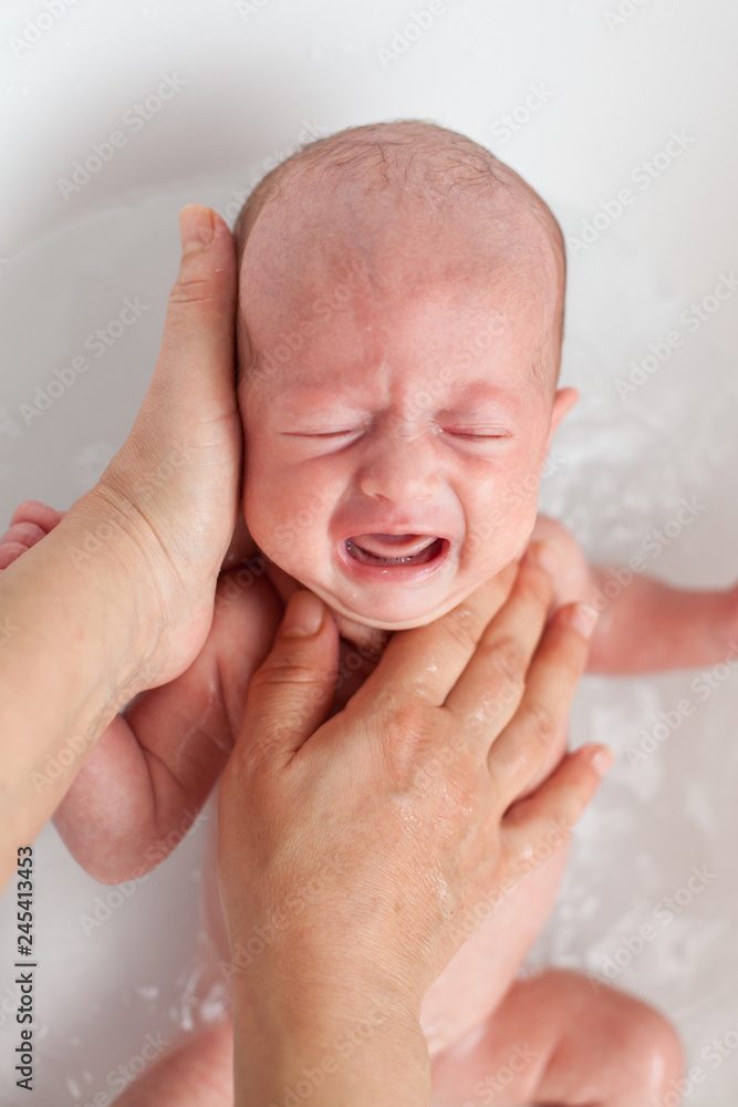 Newborn baby is being bathed by his mother. Newborn baby crying in bath time Newborn baby is being bathed by his mother. Newborn baby crying in bath time