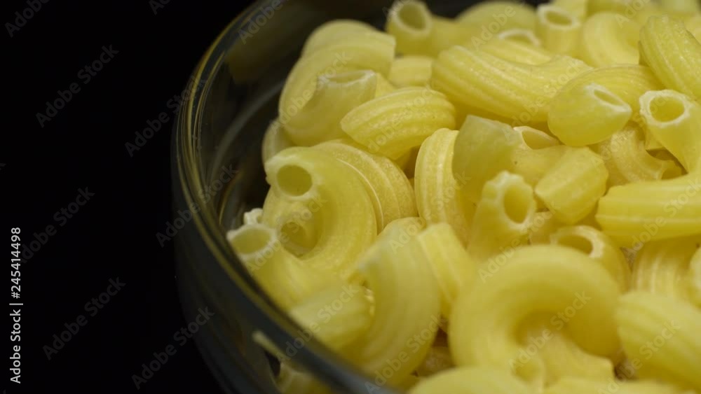 Raw macaroni in rotation. Elbow macaroni. Macaroni rigati close up. Raw pasta black background. Italian cuisine concept. Raw macaroni in rotation. Elbow macaroni. Macaroni rigati close up. Raw pasta black background. Italian cuisine concept.