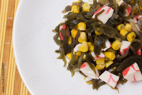 Salad of sea cabbage with crab and corn on a white plate