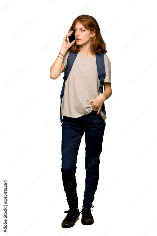 A full-length shot of a Young redhead student keeping a conversation with the mobile phone over isolated white background A full-length shot of a Young redhead student keeping a conversation with the mobile phone over isolated white background
