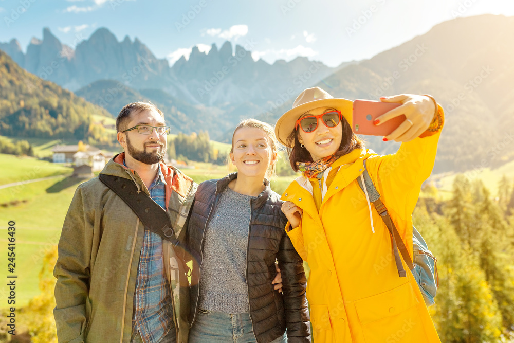 Active three friends travel and taking selfie photo during autumn holiday and vacation in the mountains of the Dolomites in the Bolzano region in Italy