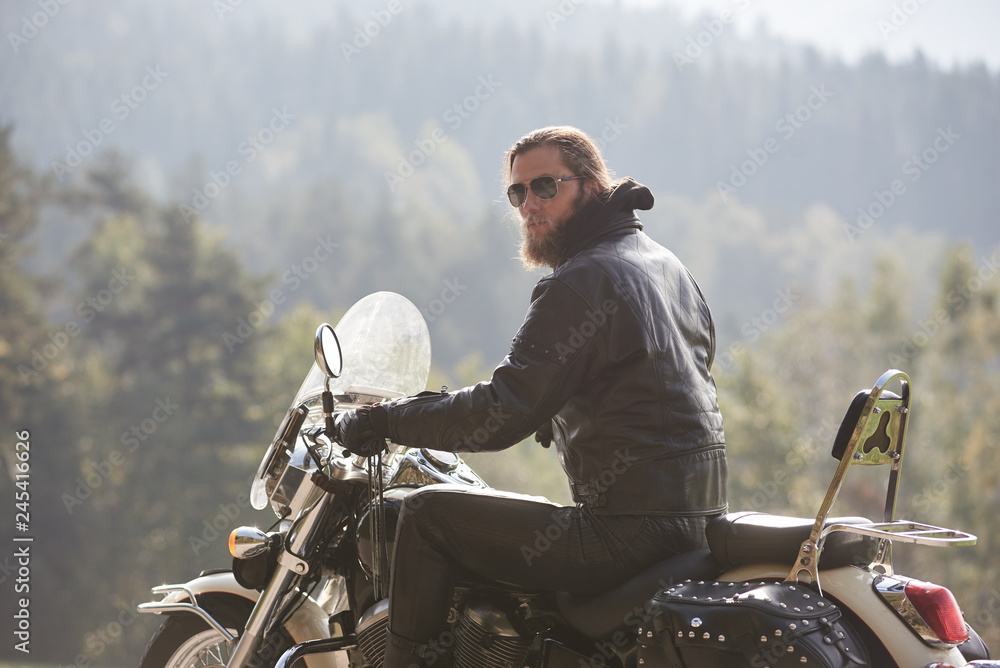 Back view of bearded motorcyclist with long hair in black leather