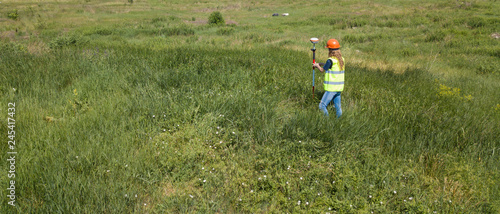 Professional Female Land Surveyor Measures Ground Control Point Using a GPS Rover. Green Field on a Background.