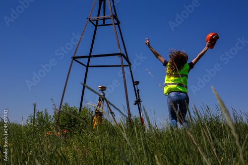Professional Female Land Surveyor Measures Ground Control Point Using a GPS Rover. Green Field on a Background. Happy Woman Finish the Work.