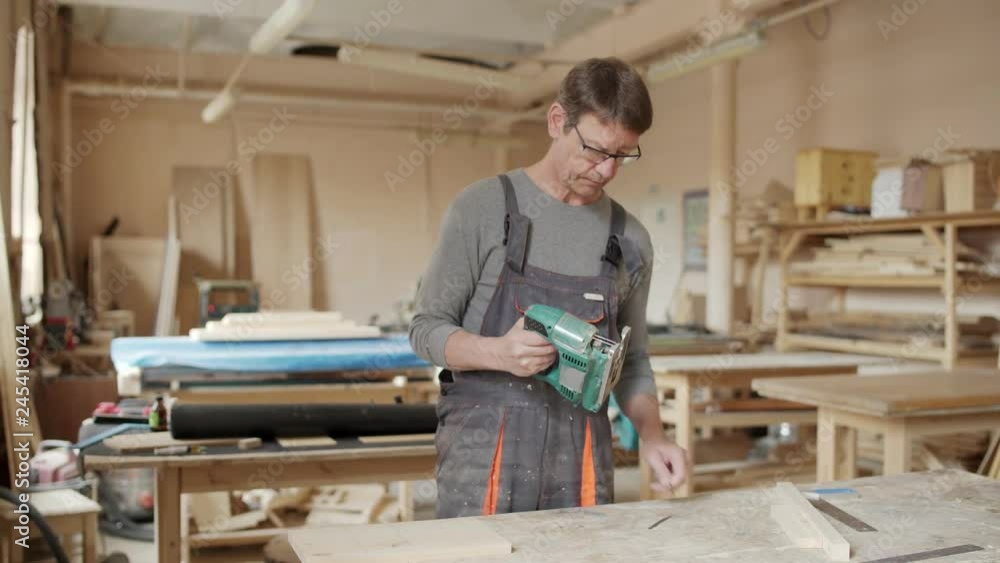 Experienced carpenter standing at workbench and placing blade into speed jigsaw Experienced carpenter standing at workbench and placing blade into speed jigsaw