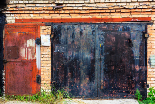 Old grunge metal doors of garage made of bricks with plants grew around on spring summer season vintage retro style