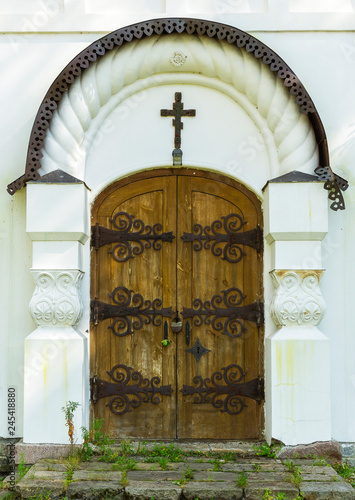 Old ancient gothic wooden church door with metal ornaments and cross on it