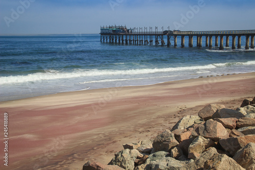 Pier on the Atlantic Ocean in Swakompund, Namibia. Beautiful pink sand, waves and stones on a sunny bright day. photo