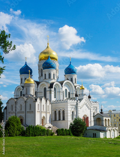 Transfiguration Cathedral at Nikolo Ugreshskiy Monastery old historical white church with blue gold domes on a spring summer day with blue cloudy sky, green grass, plants and trees