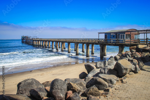 Pier on the Atlantic Ocean in Swakompund, Namibia. Beautiful pink sand, waves and stones on a sunny bright day. © Tanya Hendel