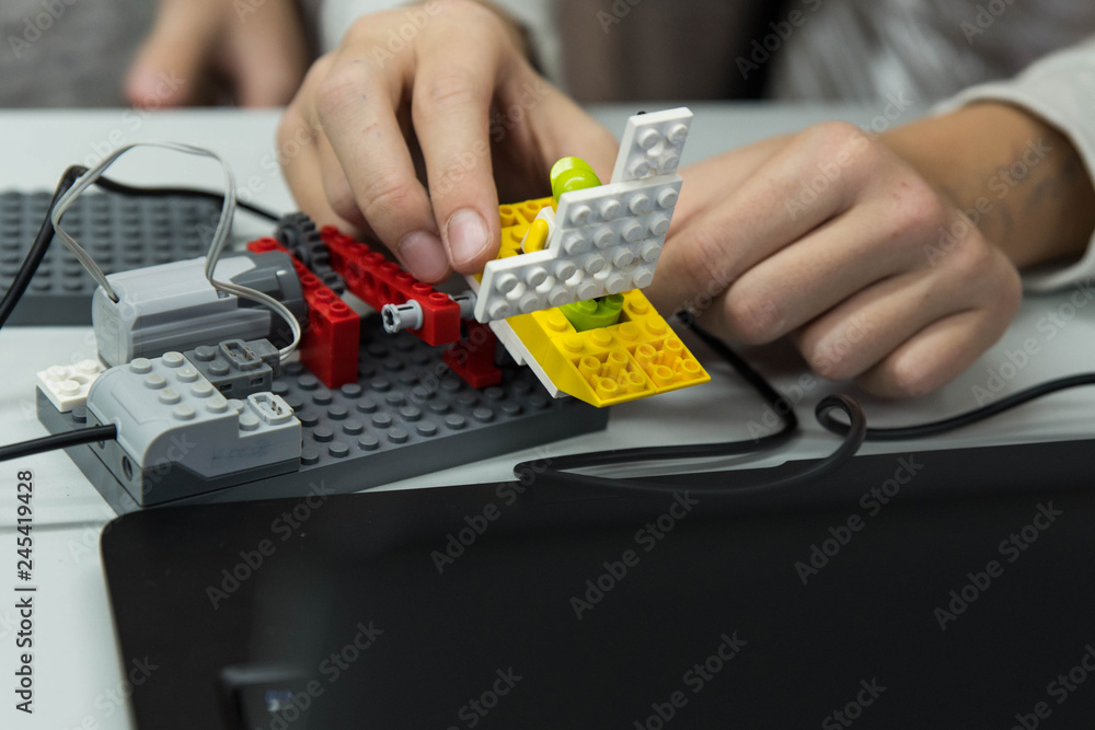 Group of kids building robot constructor from the plastics details programmed on the computer, at robotics school lesson. Education, children, technology, science and futuristic concept. E-learning. 