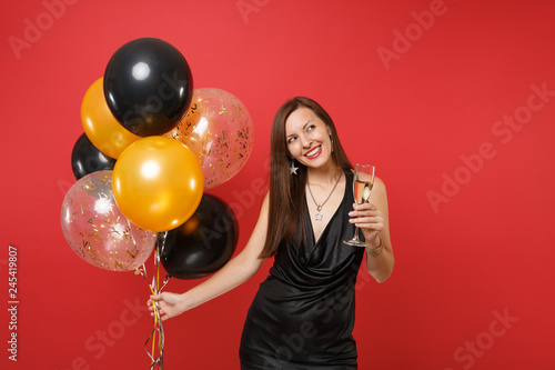 Pretty woman in black dress celebrating looking up holding glass of champagne air balloons isolated on red background. International Women's Day, Happy New Year, birthday mockup holiday party concept. © ViDi Studio