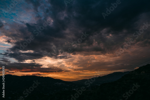 Dramatic purple and orange cloudy sunset with blue sky over mountain silhouette
