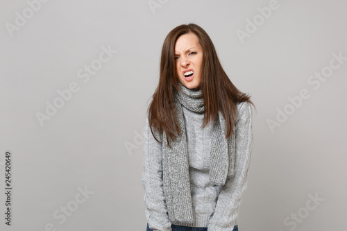 Prostrate exhausted irritated young woman in gray sweater, scarf isolated on grey background studio portrait. Healthy fashion lifestyle people sincere emotions cold season concept. Mock up copy space.