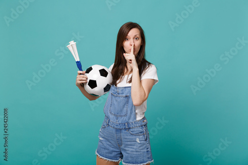 Serious woman football fan support favorite team with soccer ball, pipe say hush be quiet with finger on lips shhh gesture isolated on blue turquoise background. People emotions sport family concept. © ViDi Studio