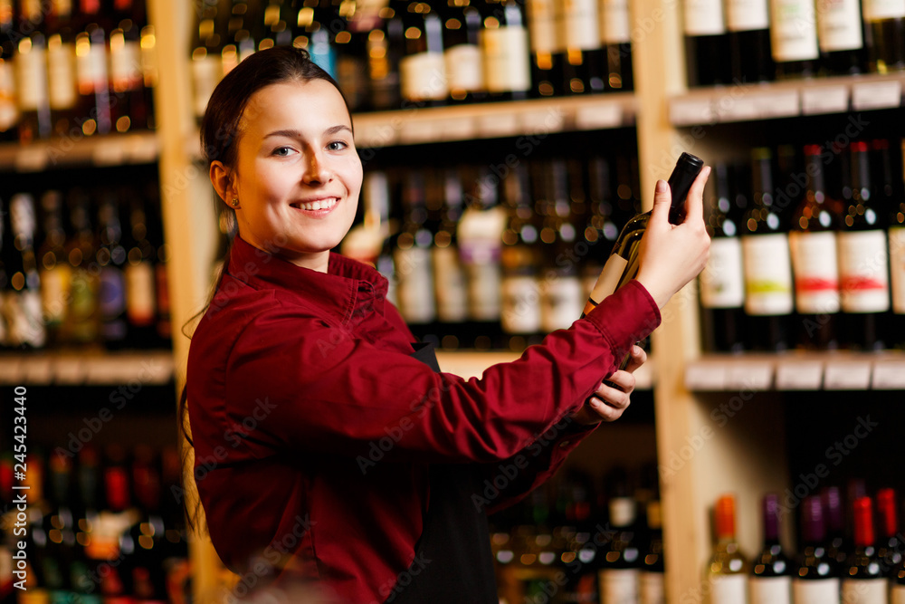 Picture of young woman with bottle in her hands in wine shop