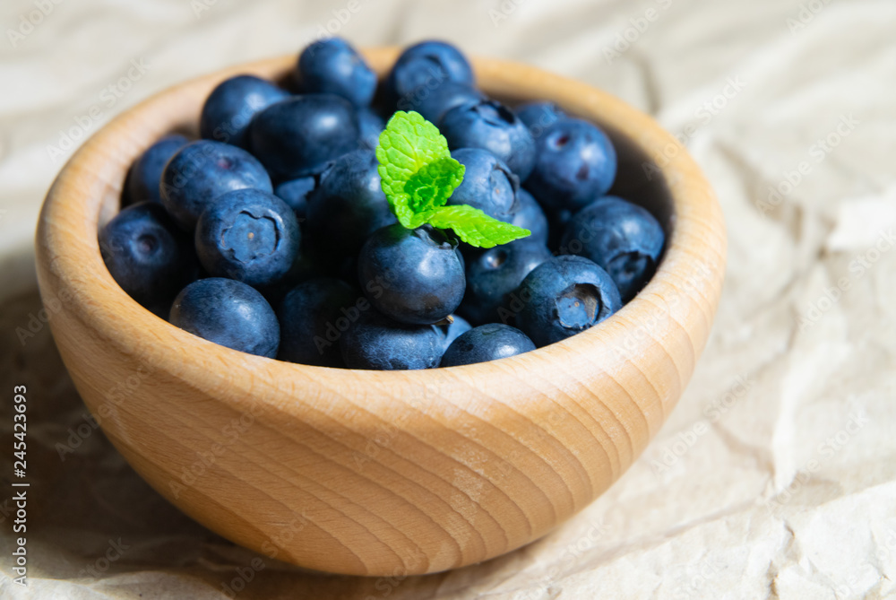 A wooden bowl full of blueberries with plain soft background decorated by fresh mint A wooden bowl full of blueberries with plain soft background decorated by fresh mint