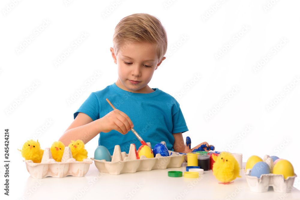 The child is painting Easter eggs. The boy is sitting at a table with colorful paints, his hands are dirty. She is happy, preparing for Easter. White isolated. The child is painting Easter eggs. The boy is sitting at a table with colorful paints, his hands are dirty. She is happy, preparing for Easter. White isolated.
