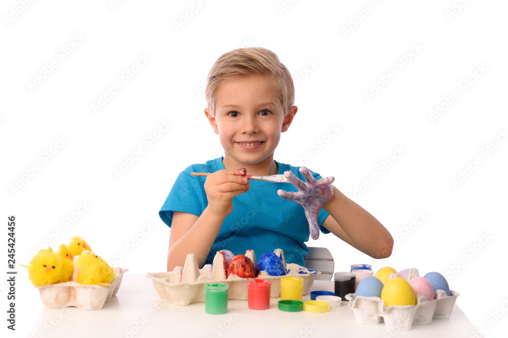 The child is painting Easter eggs. The boy is sitting at a table with colorful paints, his hands are dirty. She is happy, preparing for Easter. White isolated. The child is painting Easter eggs. The boy is sitting at a table with colorful paints, his hands are dirty. She is happy, preparing for Easter. White isolated.
