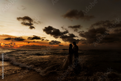 Silhouettes of the bride and groom hugging on the beach at sunset standing in the sea water