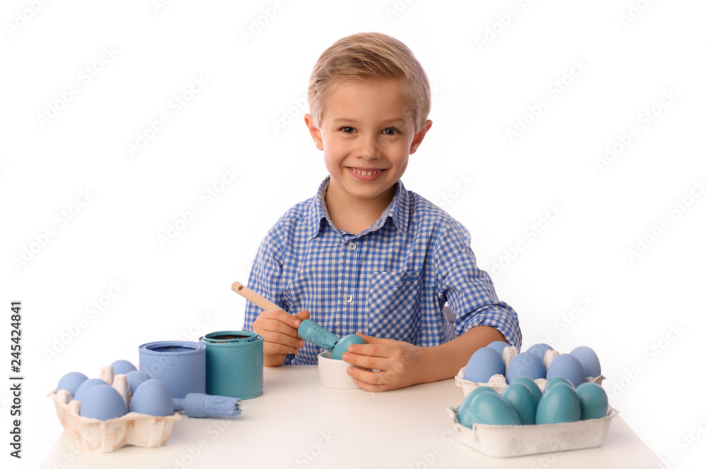 The child is painting eggs for Easter day. Nice, smiling boy sitting at a table with colorful eggs in baskets, yellow chicks. Happy Easter. Isolated on a white. The child is painting eggs for Easter day. Nice, smiling boy sitting at a table with colorful eggs in baskets, yellow chicks. Happy Easter. Isolated on a white.