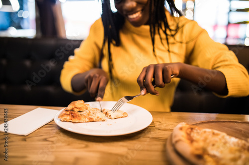 Young pretty afro american woman wearing in yellow sweater eating pizza in cafe