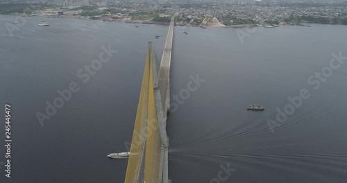 High aerial above the cable-stayed Rio Negro Bridge that links the cities of Manaus and Iranduba in the Brazilian Amazon as a boat passes underneath the bridge followed by its wake and traffic crosses photo