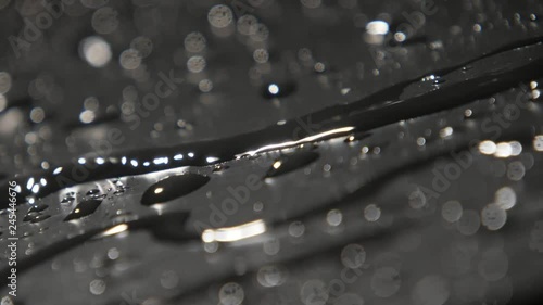 Thin runlet of rainy water creeping among splashing spots in slow motion