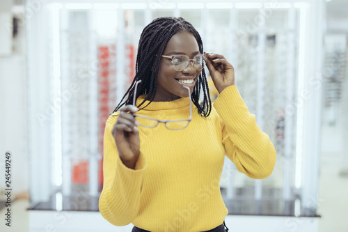 Young pretty african woman choosing between two eyeglasses frames in Optician shop photo