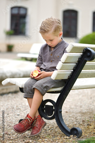 Boy stylish,  on a park bench, sad head down, holding an apple, blond hair, brown shirt, short knee-length pants. photo