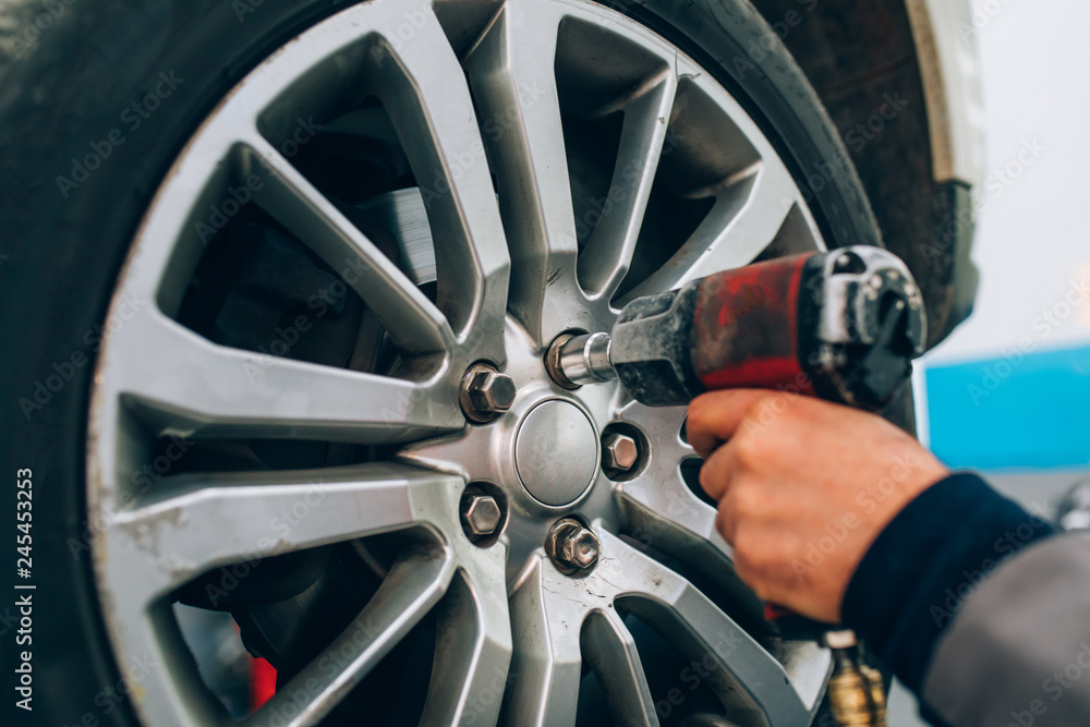 Mechanician changing car wheel in auto repair shop. Mechanic adjusting the tire wheel by using hand and tool at the repair car garage Mechanician changing car wheel in auto repair shop. Mechanic adjusting the tire wheel by using hand and tool at the repair car garage