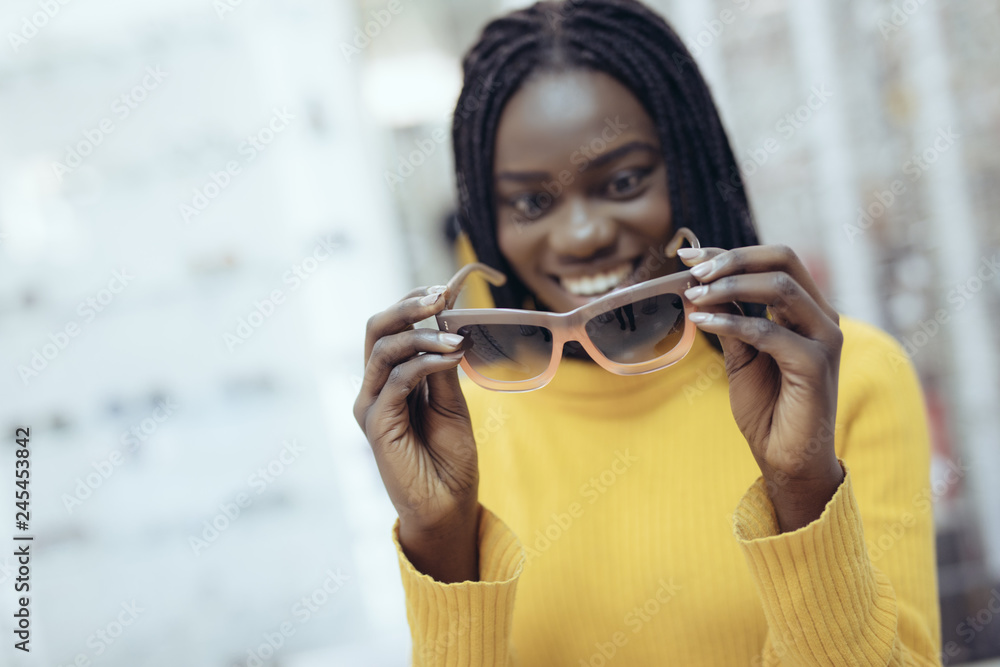 Φωτογραφία Young pretty african woman in casual clothes try different sunglasses in optical