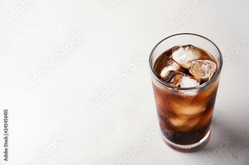 Glass of refreshing cola with ice on light table. Space for text