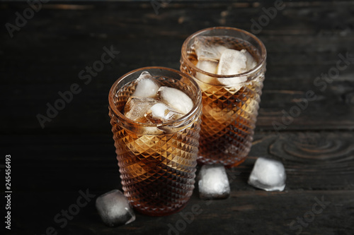 Glasses of refreshing cola with ice cubes on wooden background