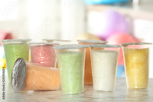 Plastic cups with cotton candy on table against blurred background