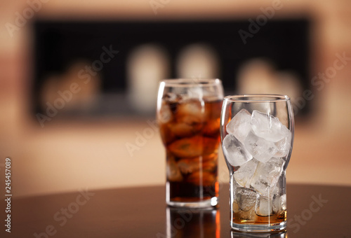 Glasses with cola and ice cubes on table against blurred background. Space for text